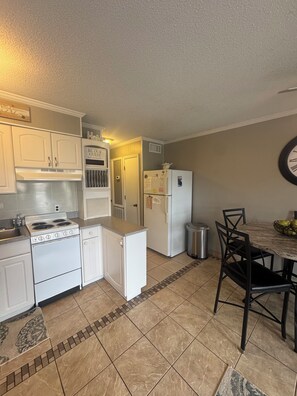 A compact kitchen with white cabinets, a stove, a refrigerator, and a dining area with a table and chairs. - Cozy 1-bedroom condo in peaceful Hilton Head Island with private beach access (Hilton Head Island)