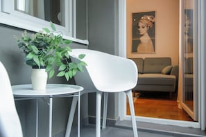 Ein modernes Wohnzimmer mit einem weißen Stuhl, einem kleinen Tisch und einem Blumentopf. Es gibt ein graues Sofa und ein Bild an der Wand.