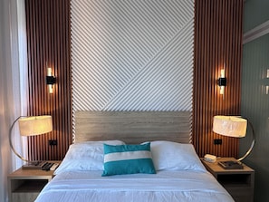 A hotel room with a bed, two bedside tables, a nightstand, a lamp, a wall-mounted light, and a patterned wall. - Apartment with an ocean view in the heart of the city (Santo Domingo)