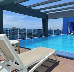 A rooftop pool with a glass barrier, a lounge chair, and a table. - Apartment with an ocean view in the heart of the city (Santo Domingo)