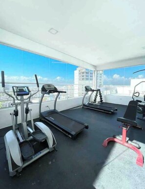 A gym with treadmills and an elliptical machine, large windows with a city view. - Apartment with an ocean view in the heart of the city (Santo Domingo)