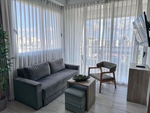 A modern living room with a grey sofa, a patterned ottoman, a wooden chair, and a small table with a remote control. - Apartment with an ocean view in the heart of the city (Santo Domingo)