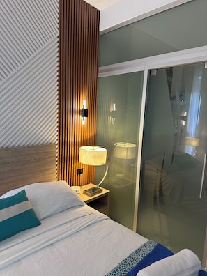 A hotel room with a bed, a nightstand with a lamp, a wooden panel wall, and a sliding glass door. - Apartment with an ocean view in the heart of the city (Santo Domingo)