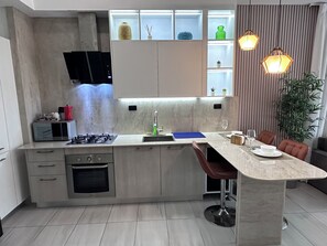 A modern kitchen with a built-in island, a gas stove, a microwave, and a sink. There is a dining area with a table and chairs. - Apartment with an ocean view in the heart of the city (Santo Domingo)