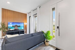 Een moderne woonkamer met een grijze bank, een flatscreen televisie, een wand van houten panelen en een groot raam.