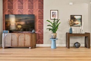A living room with a flat-screen TV, a wooden cabinet, a blue vase with a plant, and a side table with a vase and candles. - Luxury 3BR Modern Design Lake Views Vista Cay (Orlando)