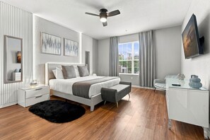 Ein modernes Schlafzimmer mit Bett, Nachttischen, Schreibtisch, Stuhl, einem schwarzen Teppich und Kunstwerken an den Wänden.