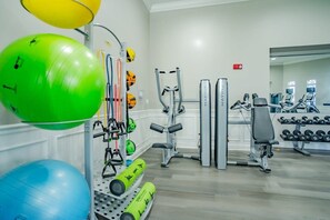 Ein Fitnessraum mit Trainingsgeräten, darunter ein grüner und blauer Übungsball, eine Gewichtbank und verschiedene Geräte.