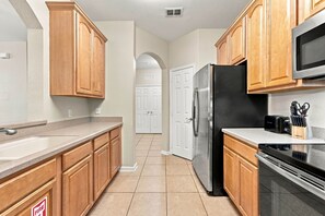 A kitchen with wooden cabinets, a stainless steel refrigerator, a microwave, and a toaster. - 3BR Vista Cay Conventions Parks and Orlando Fun (Orlando)