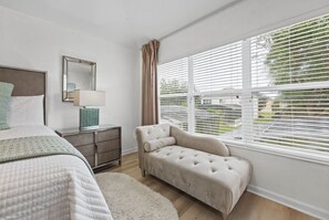 A bedroom with a bed, bedside table, lamp, and a window with blinds. - Chic 6BR Pool Themed Rooms Near Disney (Kissimmee)