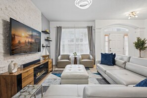 A modern living room with a flat-screen TV, a wooden entertainment unit, a beige sofa, and a coffee table. - Chic 6BR Pool Themed Rooms Near Disney (Kissimmee)