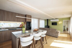 Een moderne keuken met een marmeren aanrechtblad, houten kastjes en een centraal eiland met barstoelen.