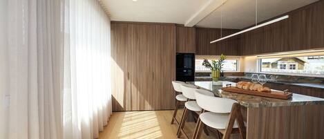 A modern kitchen with wooden cabinetry, a central island with bar stools, and a view of the city.