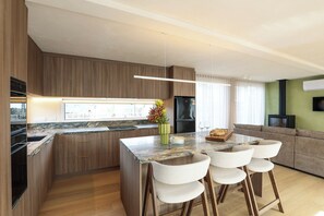 Een moderne keuken met een marmeren aanrecht, houten kastjes en een centraal kookeiland met barstoelen.