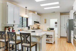 A modern kitchen with white cabinets, a central island, and a dining area with wooden chairs. - Healdsburg Couples Escape | Free Wine Tasting (Healdsburg)