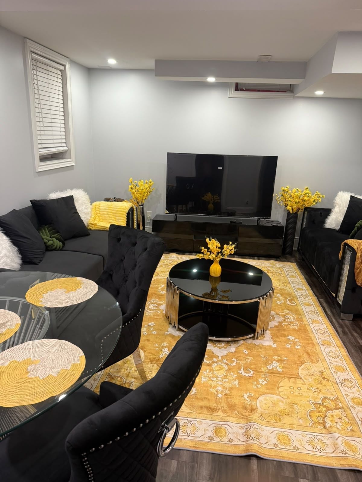 Un salon moderne avec un téléviseur à écran plat, deux canapés, une table basse et des vases décoratifs.
