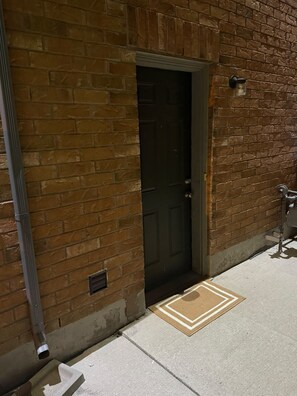 A brick building with a dark door, a metal handrail, and a doormat on the ground. - Executive Stay - Near Airport (Brampton)