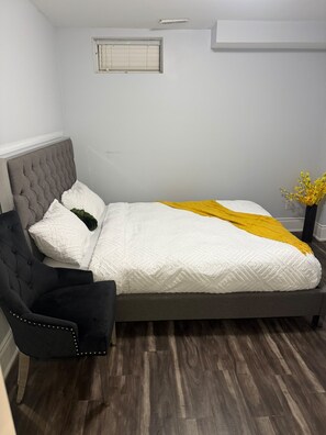 A bedroom with a bed, a chair, a window, and a wall-mounted air conditioning unit. - Executive Stay - Near Airport (Brampton)