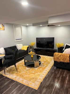 A modern living room with a black sofa, a coffee table, a TV, and a patterned rug. - Executive Stay - Near Airport (Brampton)