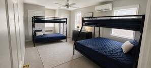 Une chambre avec deux lits superposés, un bureau, une chaise, une lampe et un ventilateur de plafond.