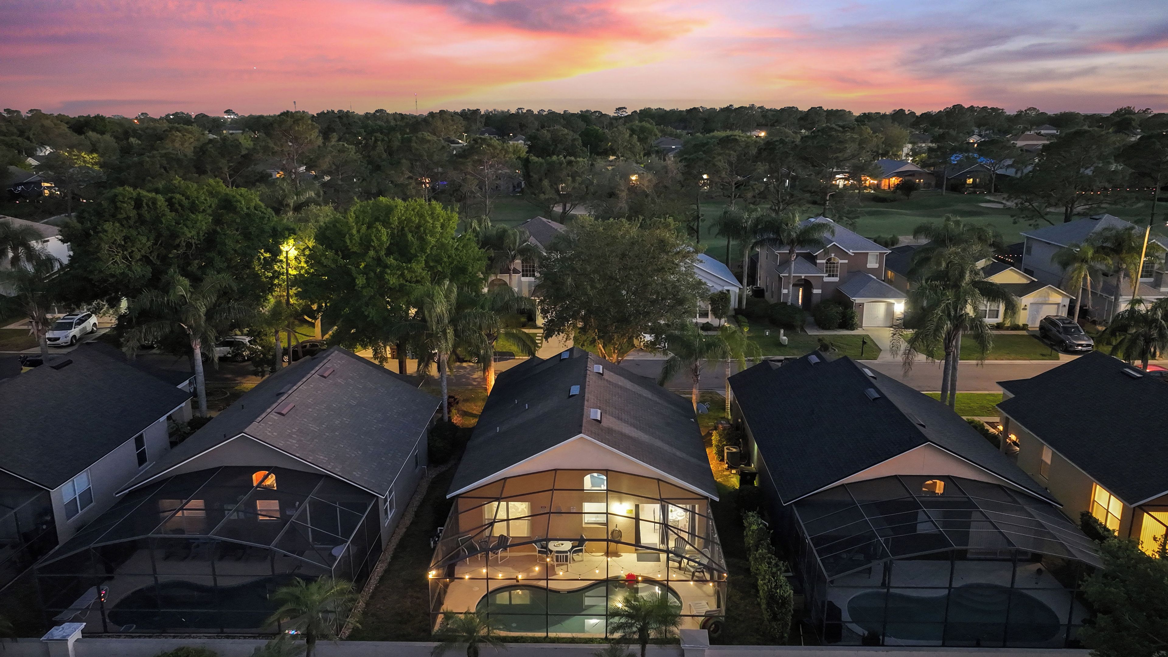 A residential area with multiple houses, a swimming pool, and a sunset sky.