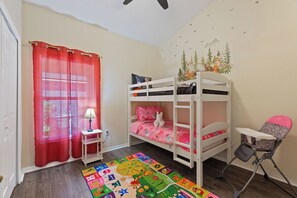A child's bedroom with bunk beds, a small table with a lamp, a colorful rug, and a high chair. - Florida Getaway-Pool and Golf Retreat near Disney (Haines City)