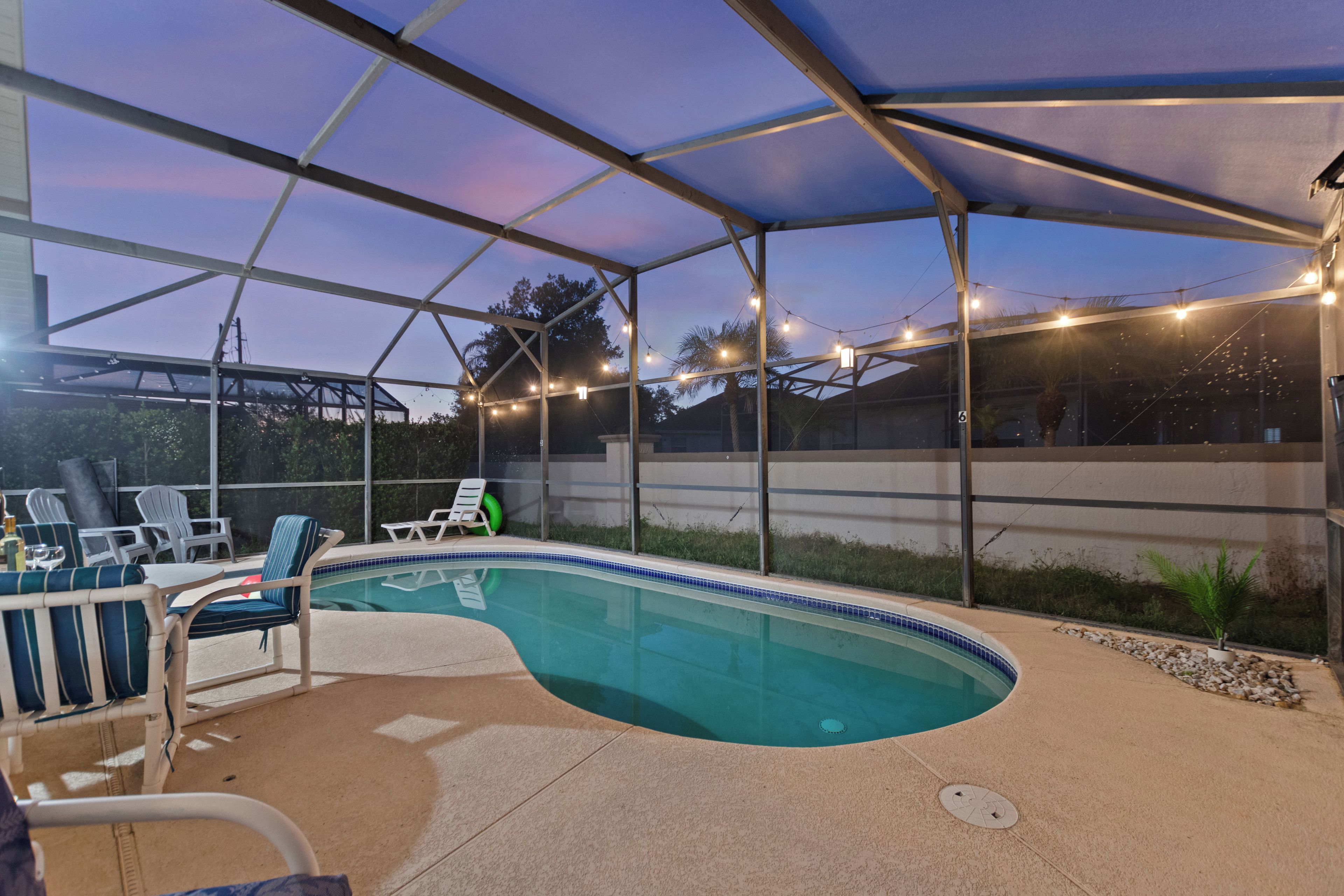 An outdoor swimming pool with lounge chairs and string lights.