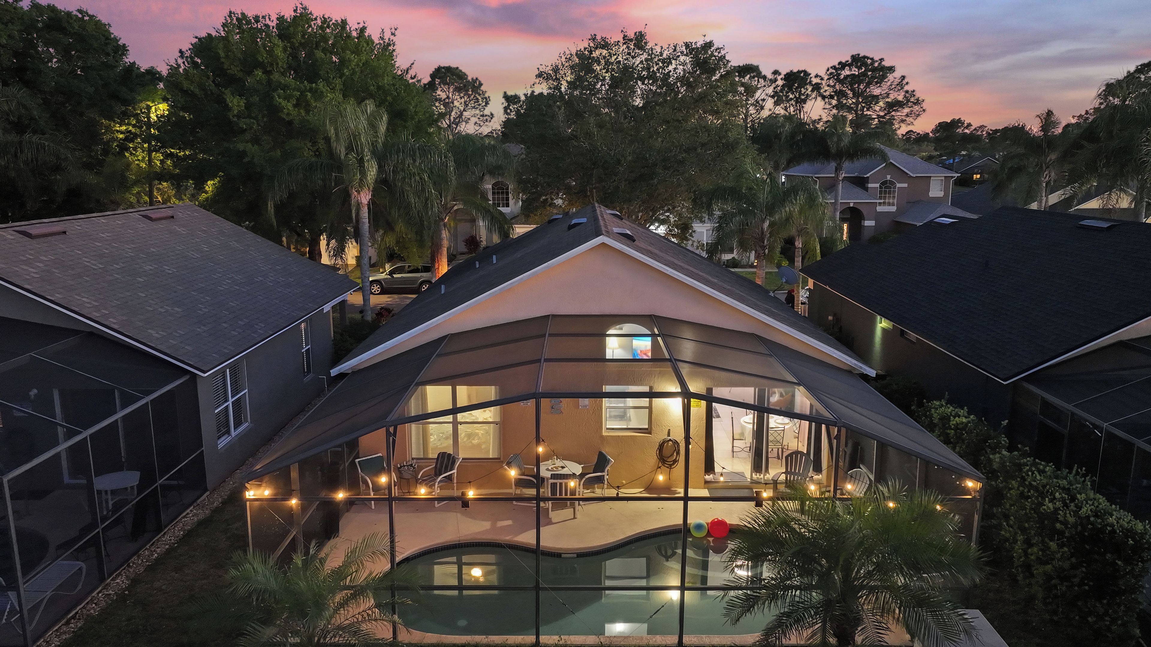 A modern house with a glass-enclosed patio overlooking a swimming pool, surrounded by trees.