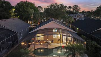 A modern house with a glass-enclosed patio overlooking a swimming pool, surrounded by trees.