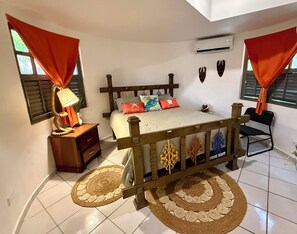 Un dormitorio con cama, mesita de noche, lámpara, cojines decorativos, arte en la pared y una silla.