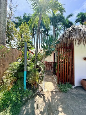 Un jardín tropical con un sendero de piedra, palmeras y una estructura con techo de paja.