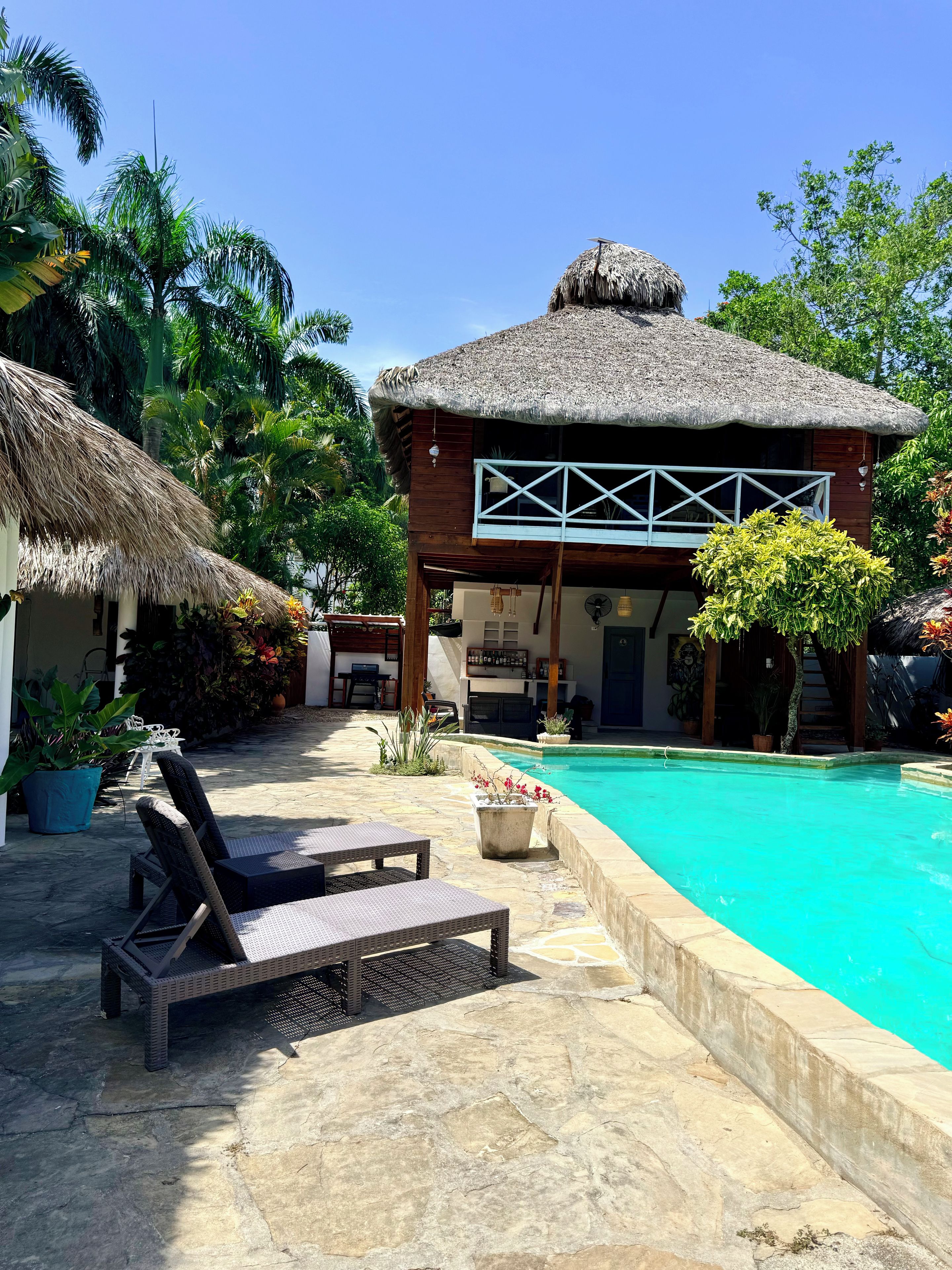 A poolside area with lounge chairs, a thatched-roof building, and a clear blue pool.