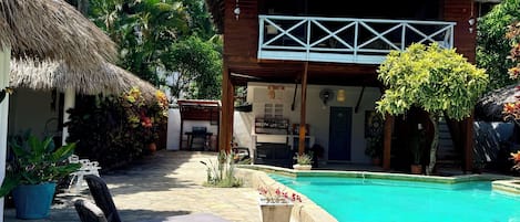 A poolside area with lounge chairs, a thatched-roof building, and a clear blue pool.