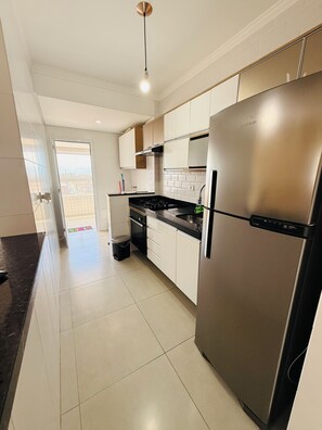 A modern kitchen with stainless steel appliances, white cabinets, and a black countertop. - Ocean View | Cozy and Steps from the Beach (Praia Grande)
