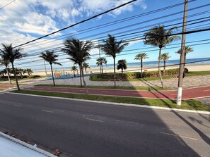 A beachside road with palm trees, a red bike path, and a view of the ocean. - Ocean View | Cozy and Steps from the Beach (Praia Grande)