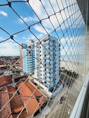 A high-rise building with multiple balconies and a view of the beach through a chain-link fence. - Ocean View | Cozy and Steps from the Beach (Praia Grande)