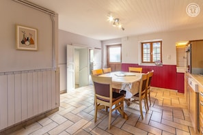A dining area with a round table, chairs, and a kitchen in the background. - The Little Warrior (CHAMBERY)