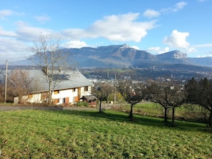 A residential area with a house, a grassy field, and mountains in the background. - The Little Warrior (CHAMBERY)
