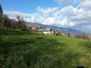 A grassy field with a house and a mountain in the background. - The Little Warrior (CHAMBERY)