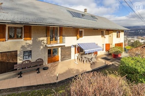 A two-story building with a balcony, a covered patio with outdoor furniture, and a view of the surrounding landscape. - The Little Warrior (CHAMBERY)