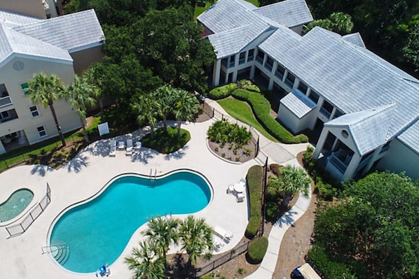 An aerial view of a residential area with a swimming pool, multiple houses, and well-maintained gardens.