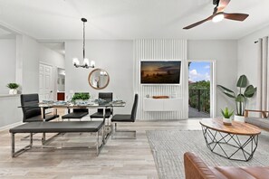 Ein modernes Wohnzimmer mit Essbereich, Deckenventilator, Flachbildfernseher und Balkon mit Pflanzen.