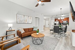 Ein modernes Wohnzimmer mit einem braunen Ledersofa, einem runden Couchtisch und einem Essbereich mit einem schwarzen Stuhl und einem Glastisch.