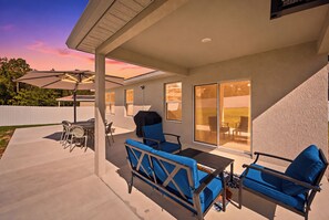 Un patio techado con mobiliario exterior, una parrilla y vistas al jardín trasero.