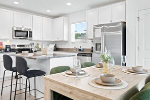 Una cocina moderna con armarios blancos, un refrigerador de acero inoxidable y una zona de comedor preparada para una comida.