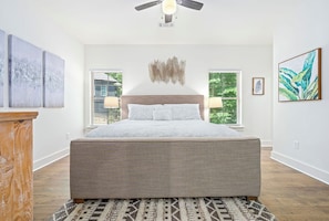 A bedroom with a large bed, two bedside lamps, a ceiling fan, and artwork on the walls. - 3 bedroom, 2 bath, with pool house, lake-access, boat slip on Lake Martin (Tallassee)