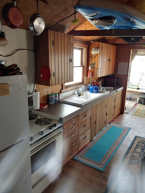 A compact kitchen with wooden cabinets, a gas stove, a microwave, and a window providing natural light.