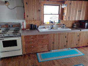 Una cocina con armarios de madera, una estufa blanca, un lavaplatos y un ventanal.