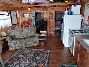 Ein gemütlicher Wohnbereich mit einer Couch, einem Fernseher, einer Küchenzeile mit Herd und Kühlschrank sowie einem Teppich mit Muster.