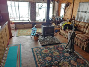 Una sala de estar acogedora con chimenea, sofá, alfombra y ventana con vistas a árboles.